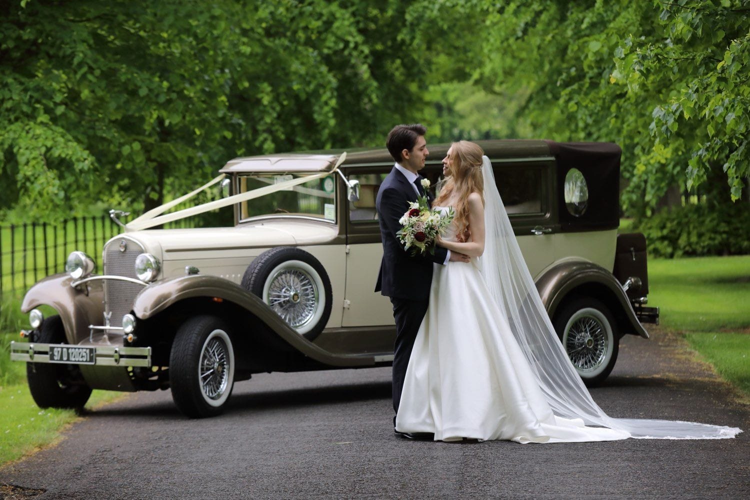 The bride and groom standing with the car behind them on the tree lined avenue of Luttrelstown Castel