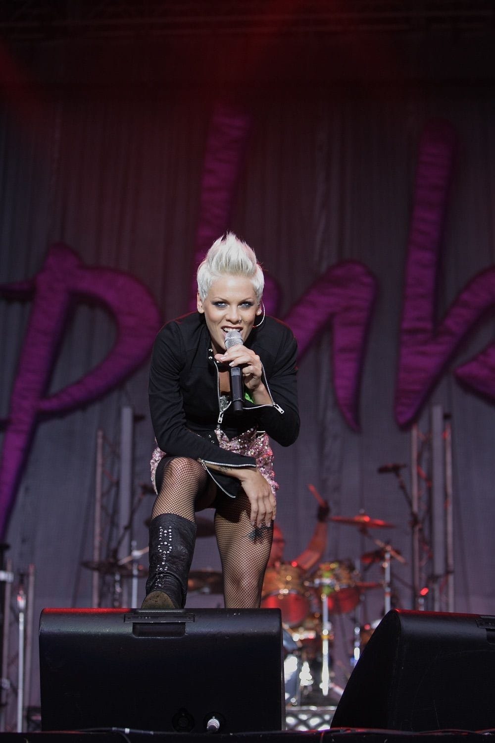 Pink onstage leaning forward with one foot up on a speaker