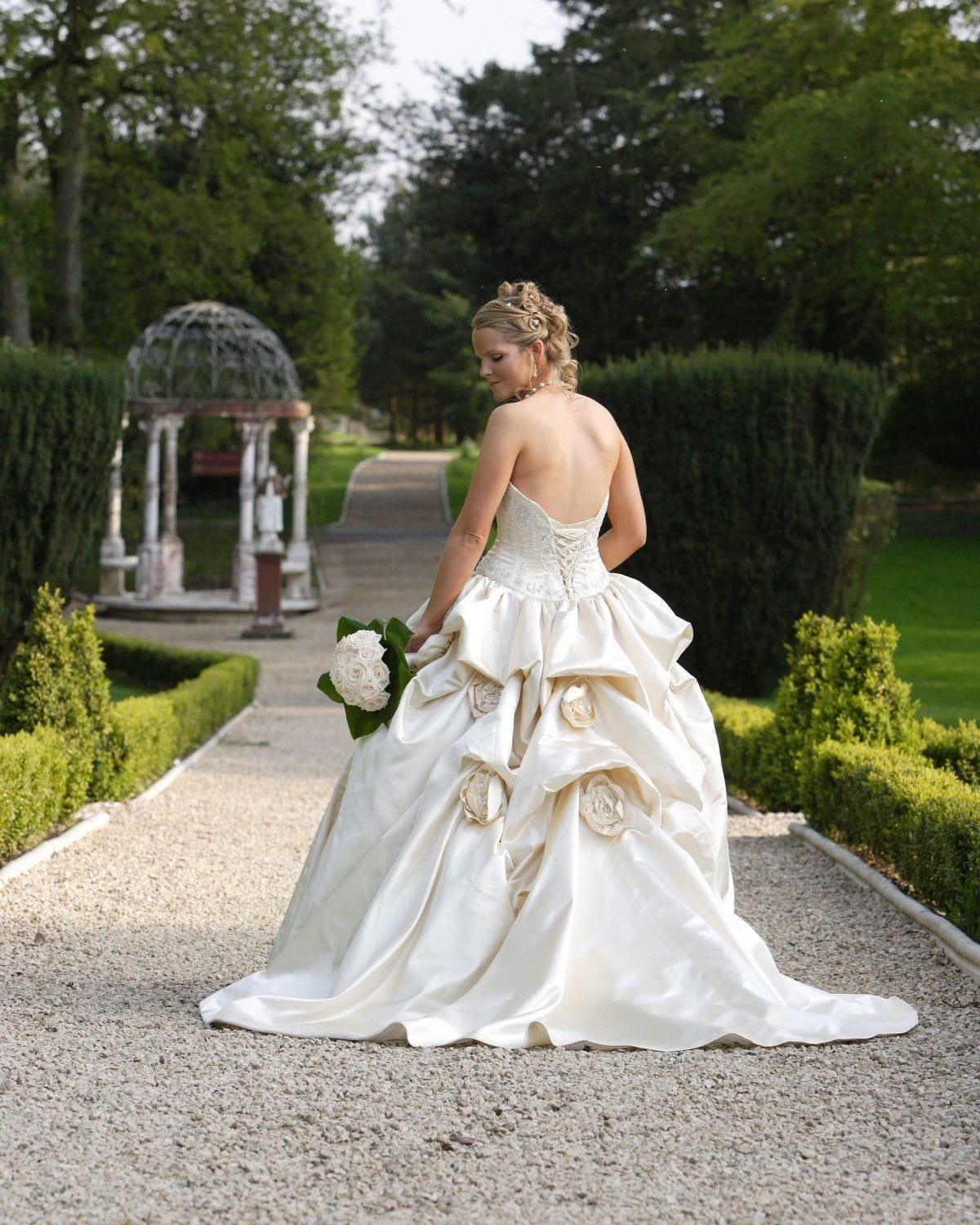 The bride stand with her back to the camera looking down to her bouquet on the garden path of the Killashee House Hotel, Naas, Co Kildare