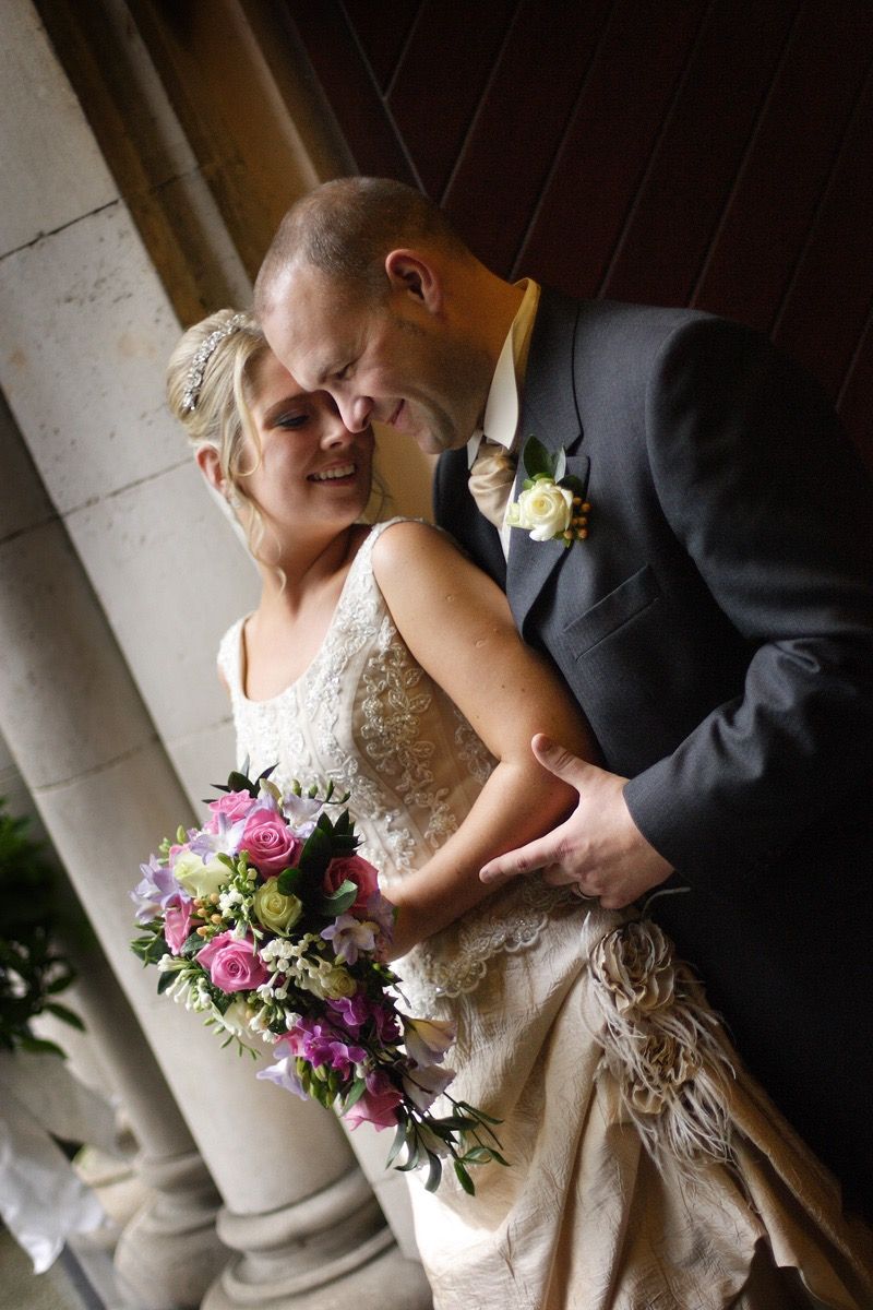 The groom holds her from behind as she turns her head back to him and rests her forhead against his and smiles