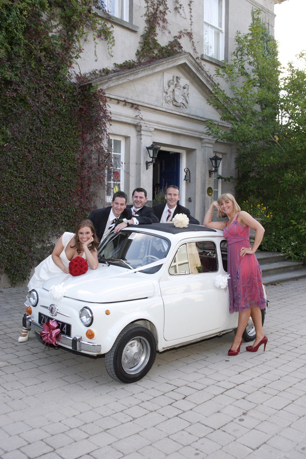 The bride, groom and some friends stand around the white Fiat 500 that they had as their bridal car