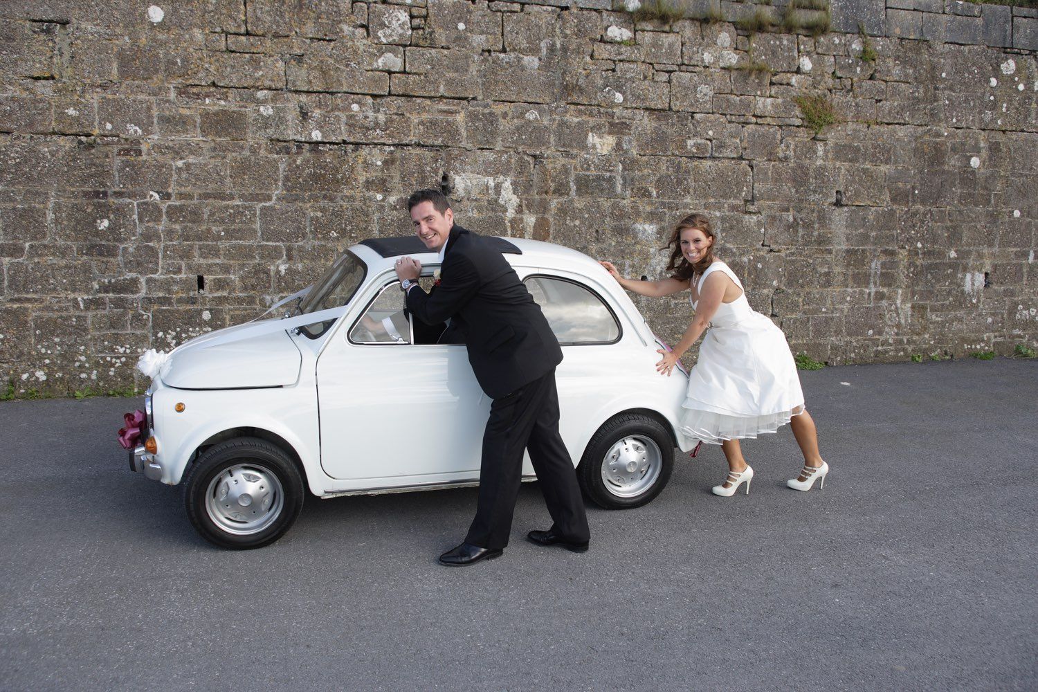 The bride and groom pretend to break down and have to push their white Fiat 500 wedding car at a Wexford wedding