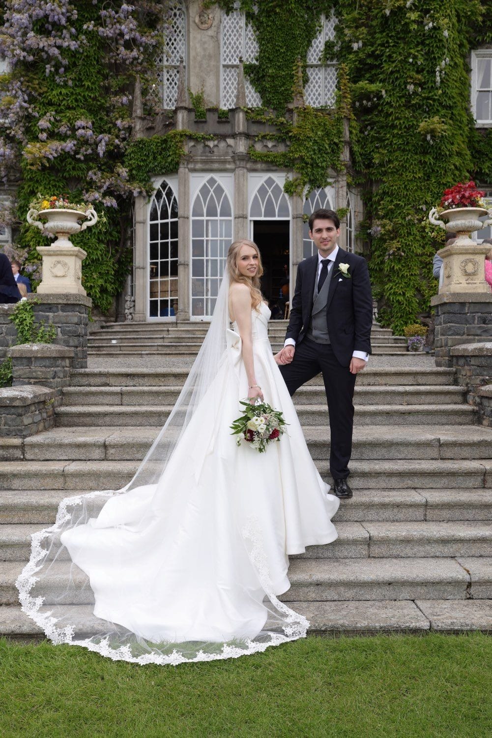 The bride and groom standing showing off the detail of her dress, on the steps up to the library of Luttrelstown Castle