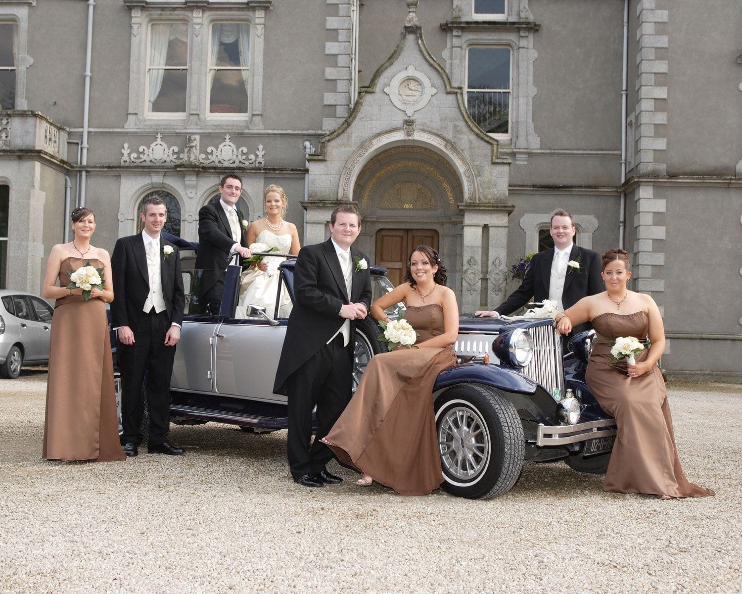 The bridal party sit and stand around the wedding car outside teh Killashess House Hotel, Co Kildare